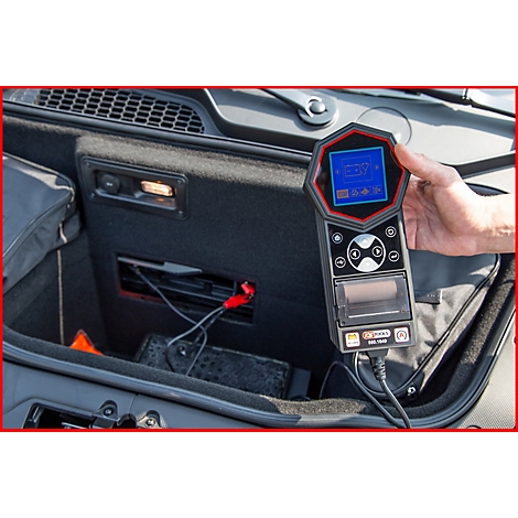 Person hält ein Diagnosegerät in der Hand, das im Kofferraum eines Autos verwendet wird. Der Bildschirm zeigt Messwerte an.